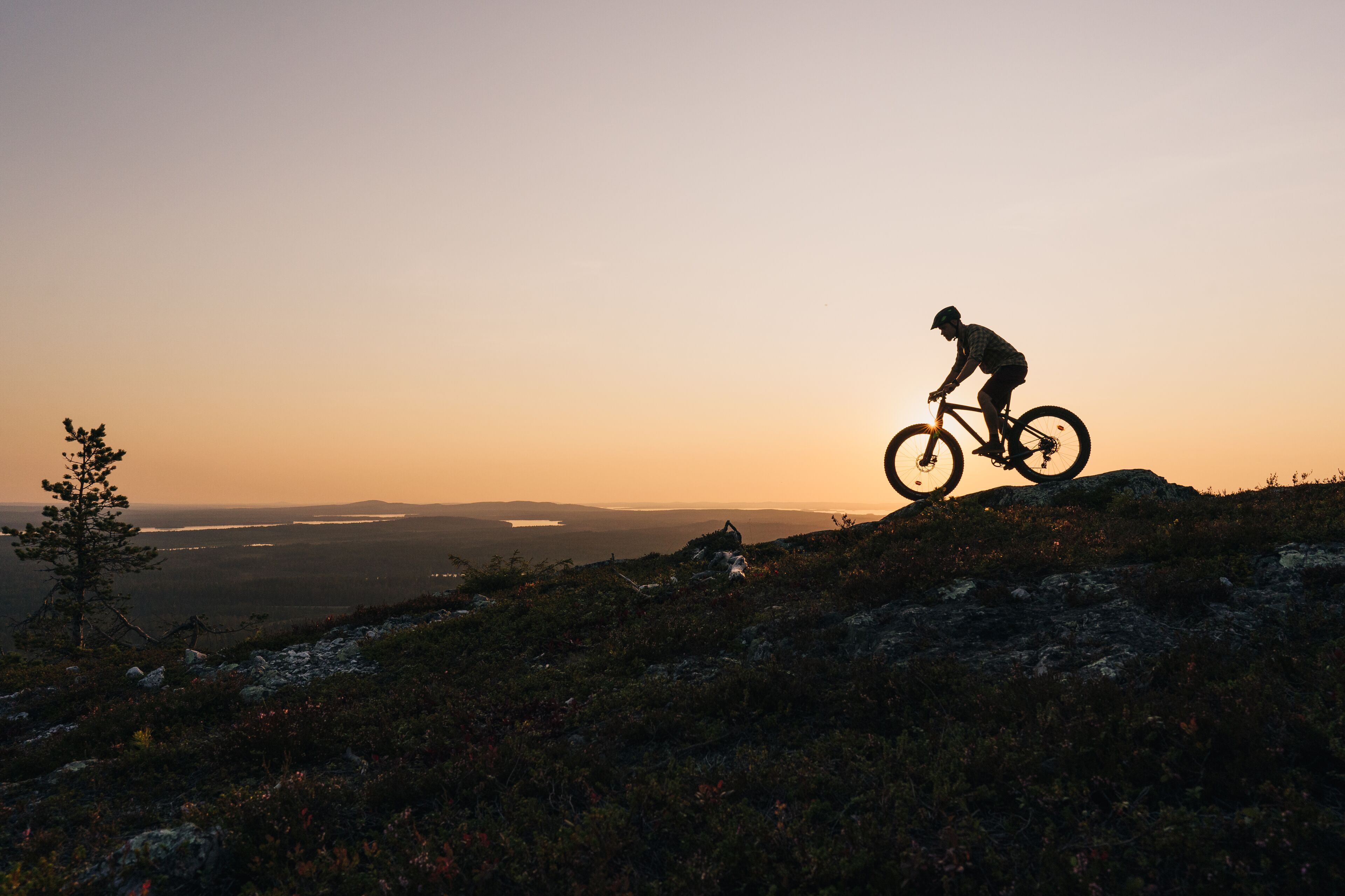 A mountain biker on a trail with a view of a valley and distant mountains during sunset.