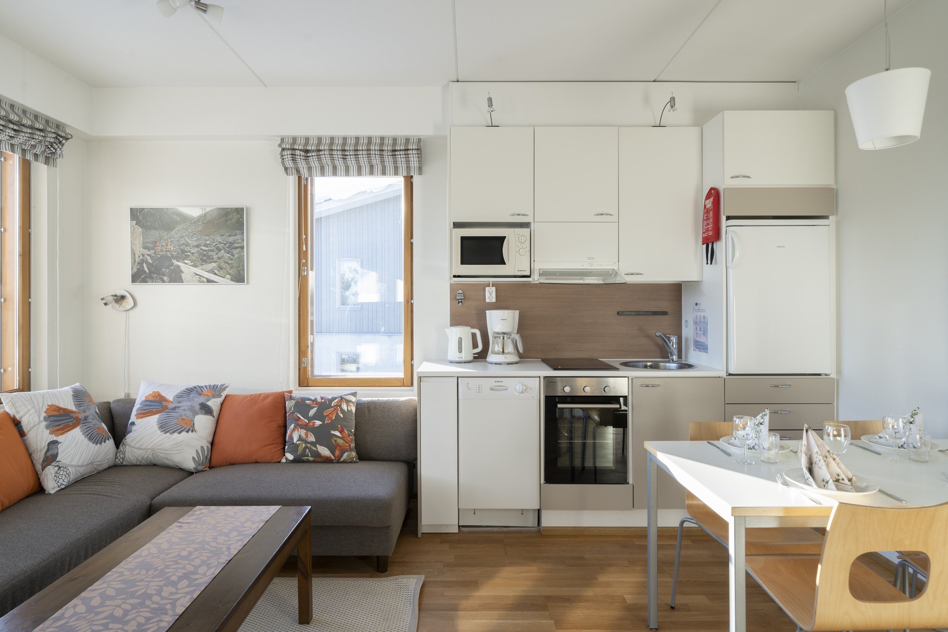 Un espacio habitable compacto con kitchenette, comedor y sofá con cojines.