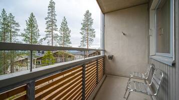 A balcony with a wooden railing, a metal bench, and a view of trees and houses.