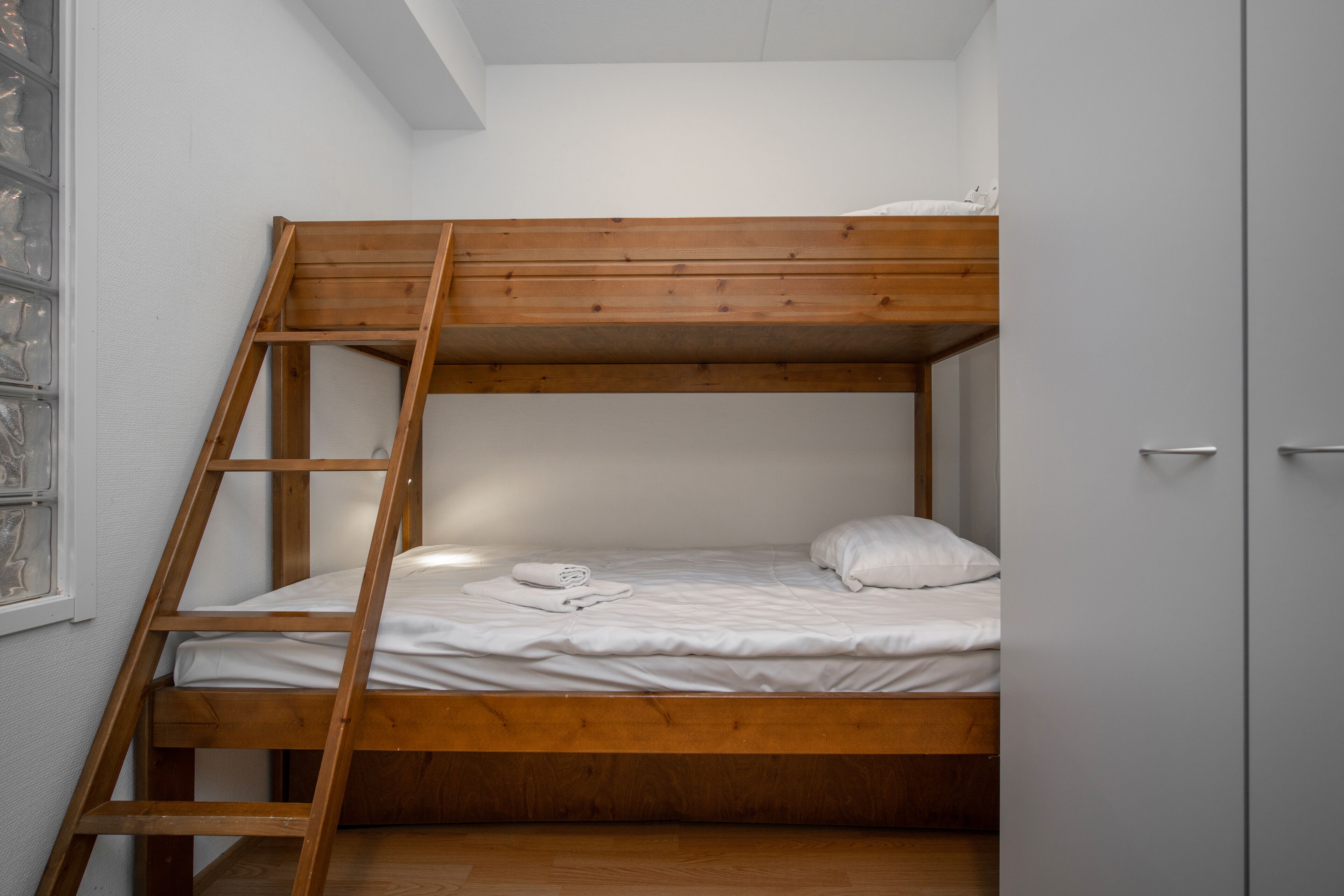 Ein Stockbett mit einer Holzleiter, weißer Bettwäsche und einem weißen Kopfkissen.