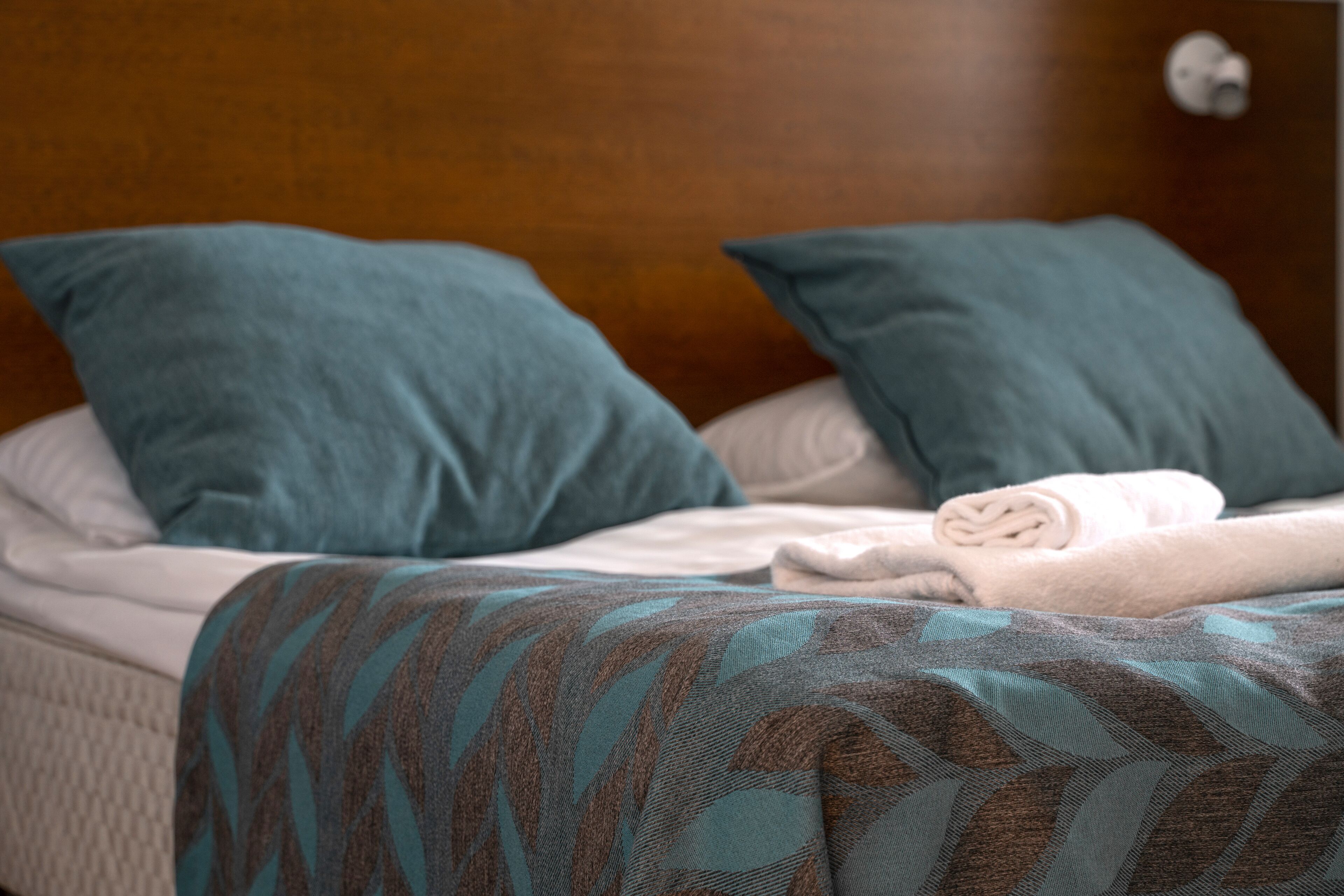 A neatly made bed with a patterned blanket, two pillows, and a folded towel.