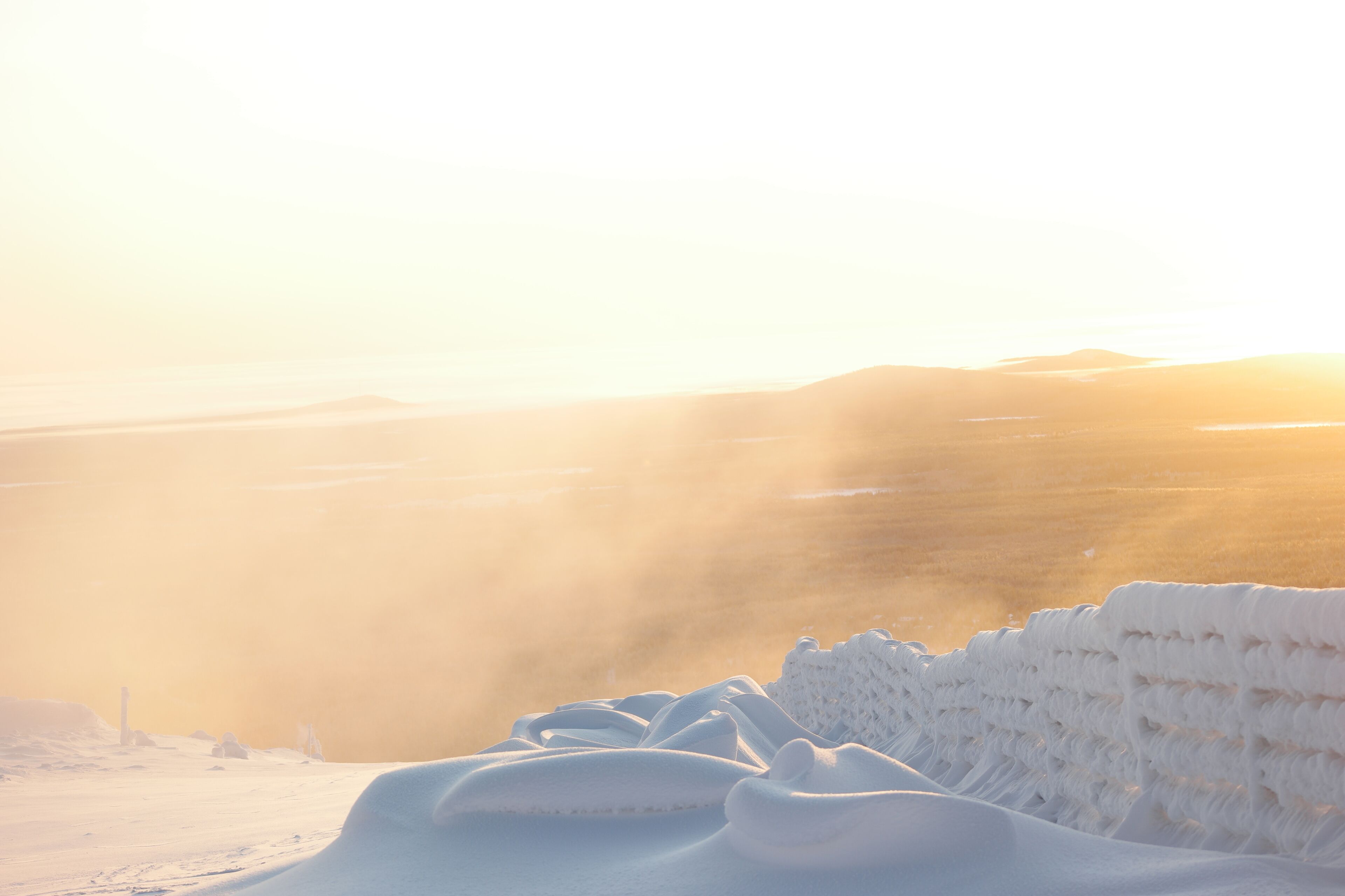 A snow-covered landscape with a distant view of a mountain range and a lighthouse.