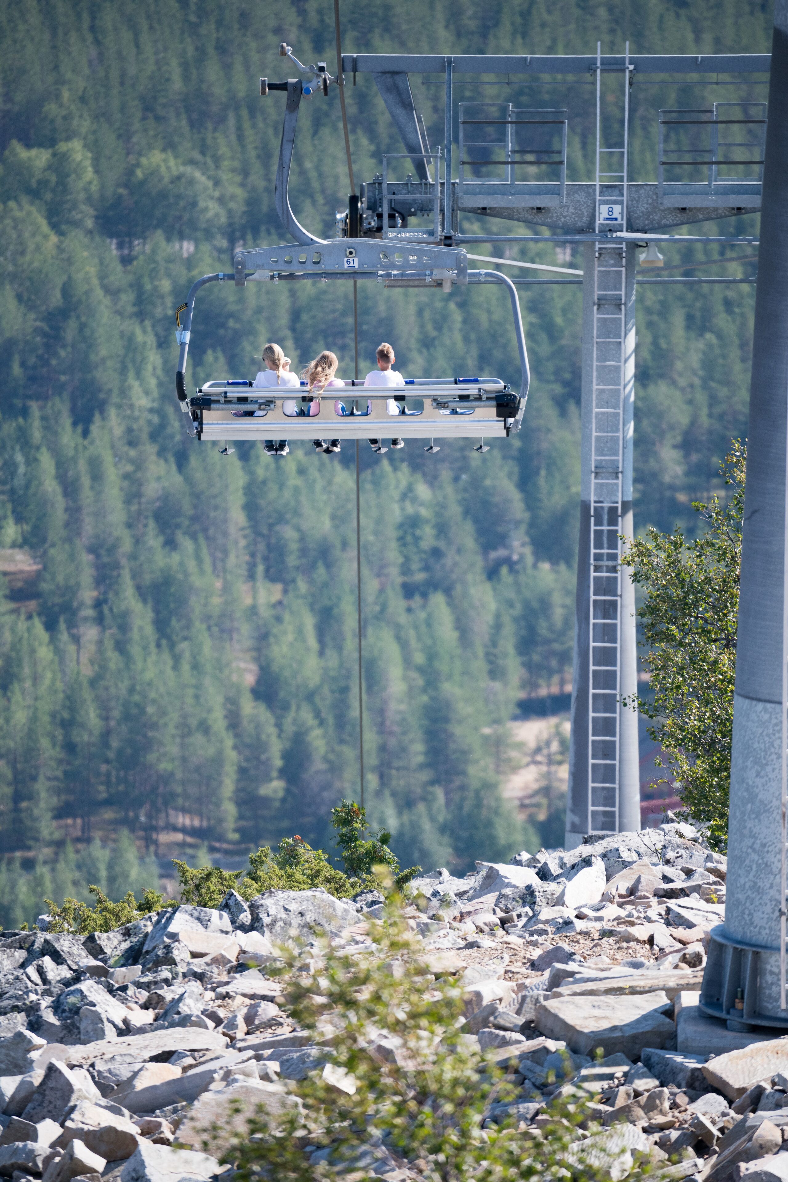 Köysirata, jossa on matkustajia, kivinen maisema ja metsäinen vuoristo taustalla.