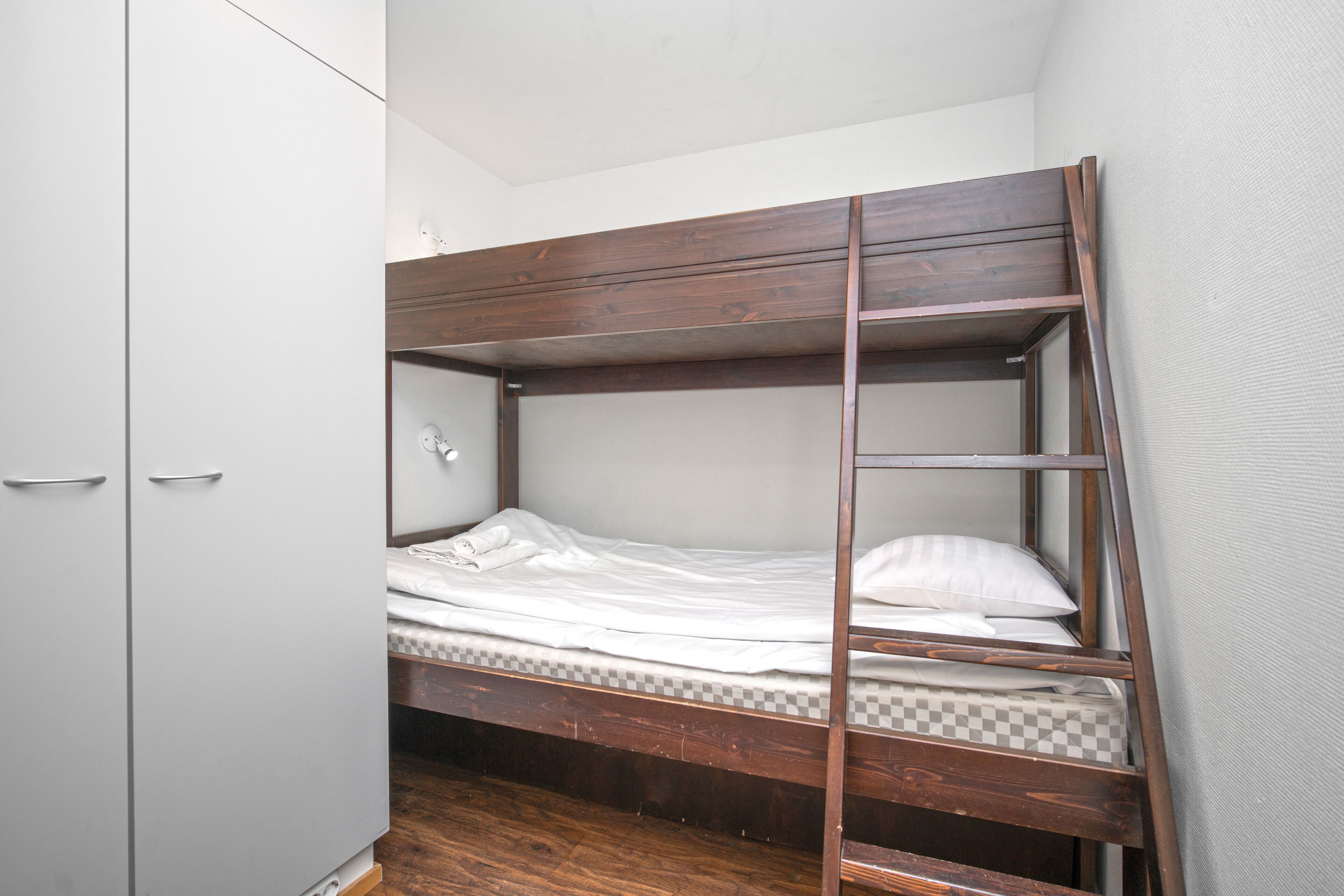 A bunk bed with a wooden frame, a white mattress, and a checkered pillow.