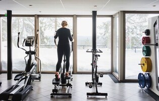 Un gimnasio con equipo cardiovascular, máquinas de pesas y grandes ventanales con vistas al exterior.