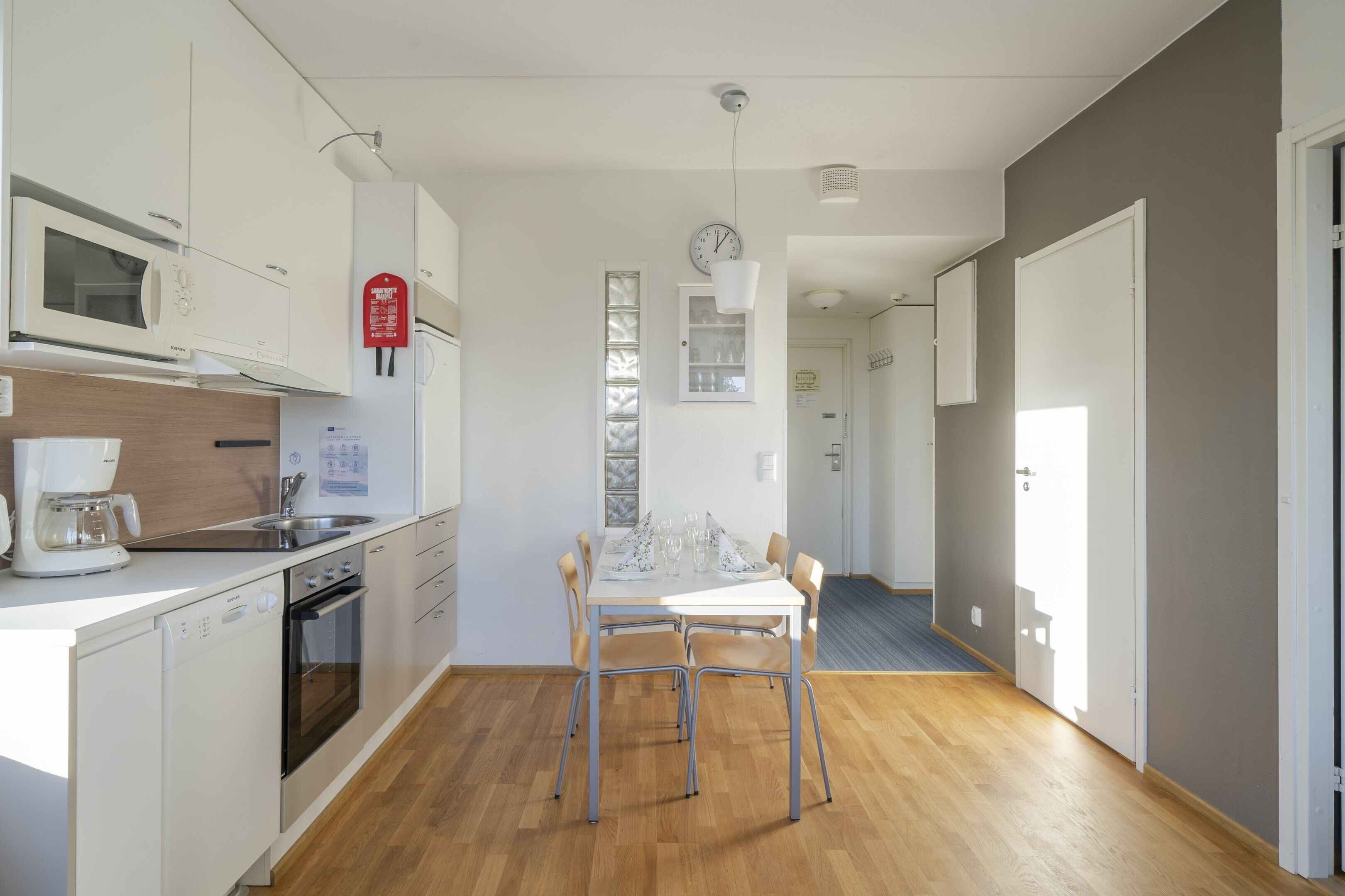 Une cuisine moderne avec des meubles blancs, un four à micro-ondes, une machine à café et une table à manger avec quatre chaises.