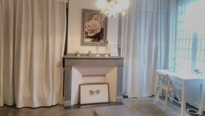 A room with a fireplace, a desk, and a chair. There is a picture frame on the mantel and a picture frame on the floor. - Au Bien Venu (Noe)