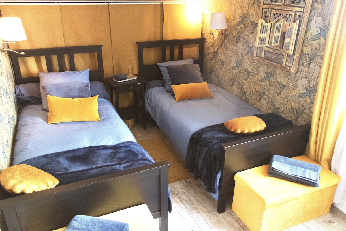 Une chambre avec deux lits, chacun doté d’une tête de lit en bois, et une petite table avec une lampe.