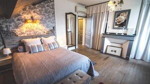 A bedroom with a large bed, a nightstand, a dresser, a mirror, and a fireplace. - Au Bien Venu (Noe)