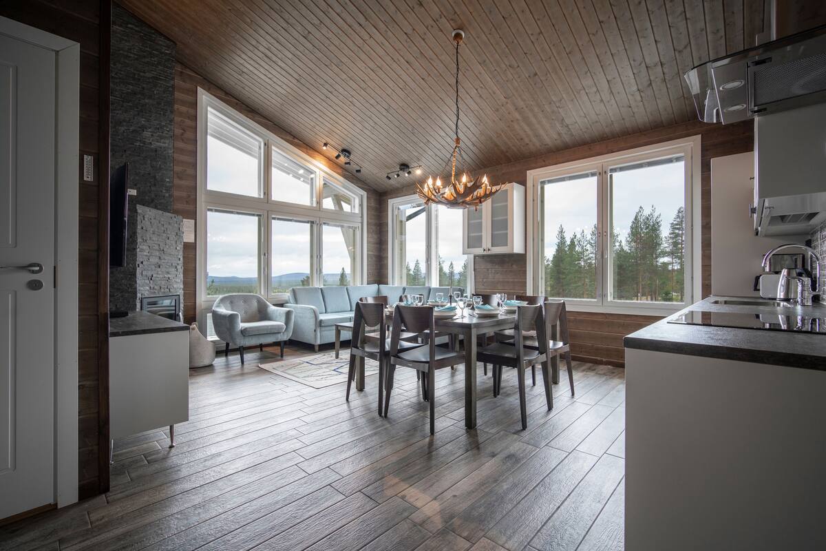 A spacious kitchen with a dining area, large windows, and a wooden ceiling.