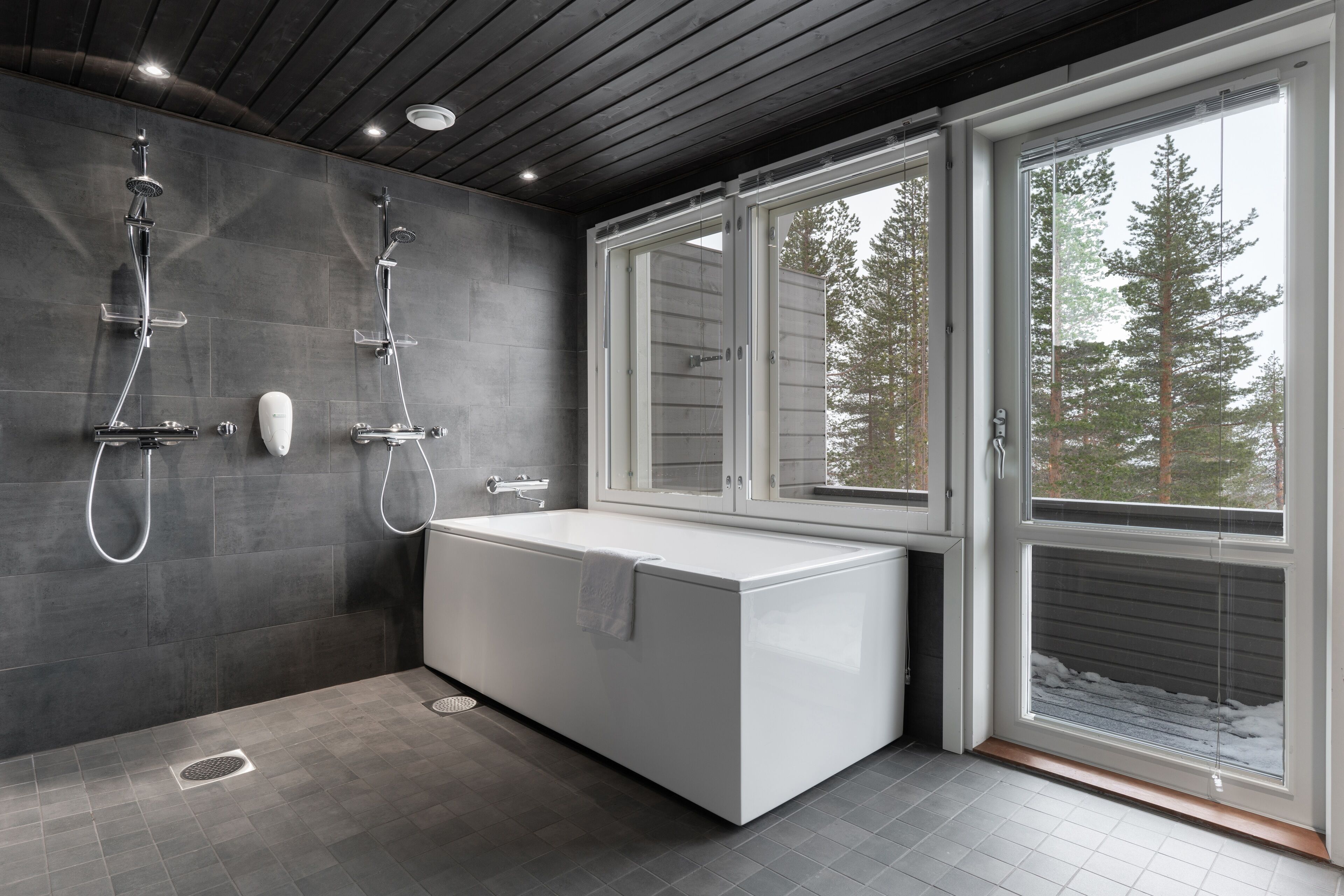 Un baño moderno con una bañera grande, dos duchas y una ventana con vista a árboles.