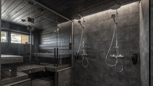 A modern shower area with a glass enclosure, a bench, and a wall-mounted showerhead. - Ski-Inn PyhäLinna (Pyhätunturi)