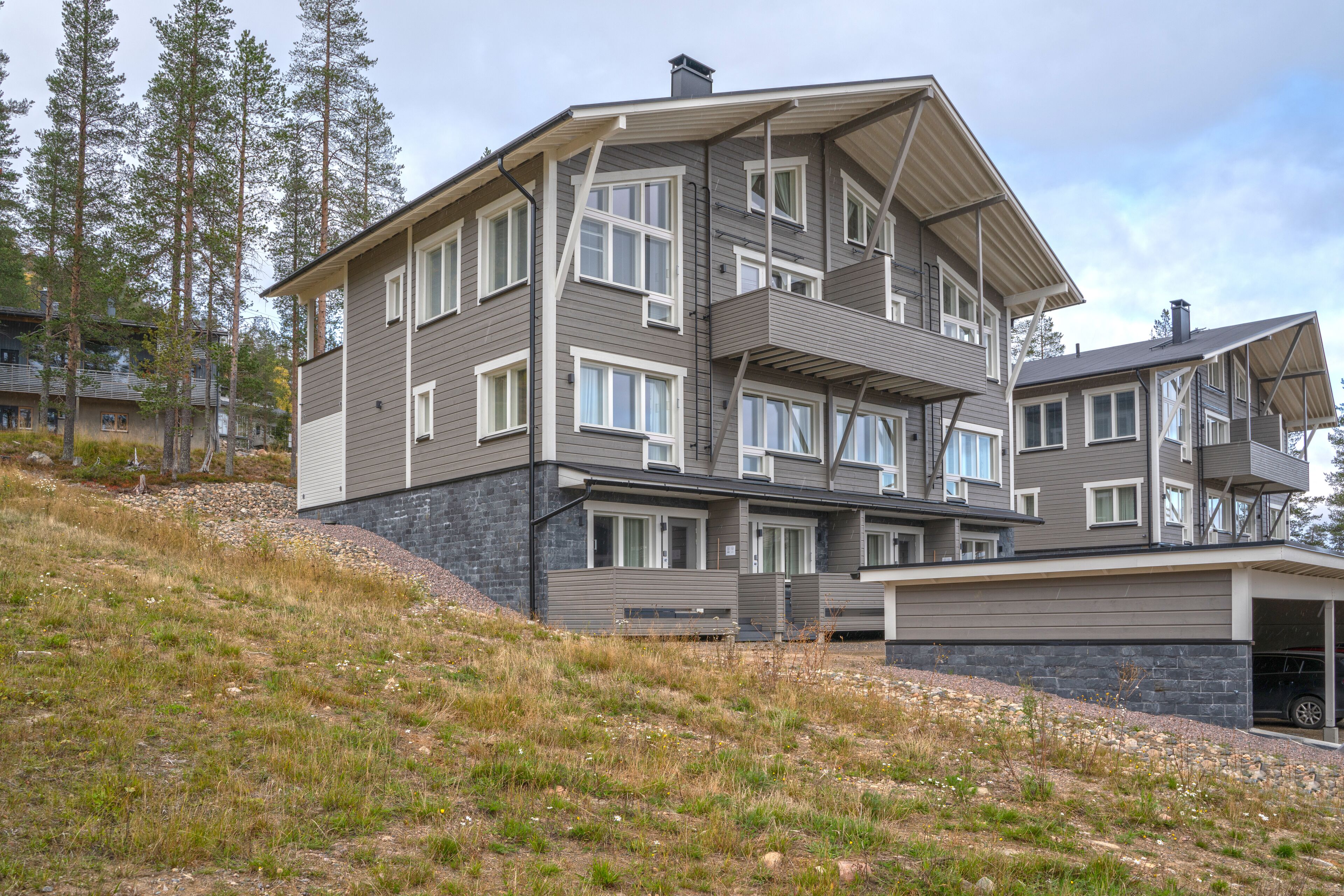 A multi-story residential building with a modern design, featuring balconies, large windows, and a stone foundation.