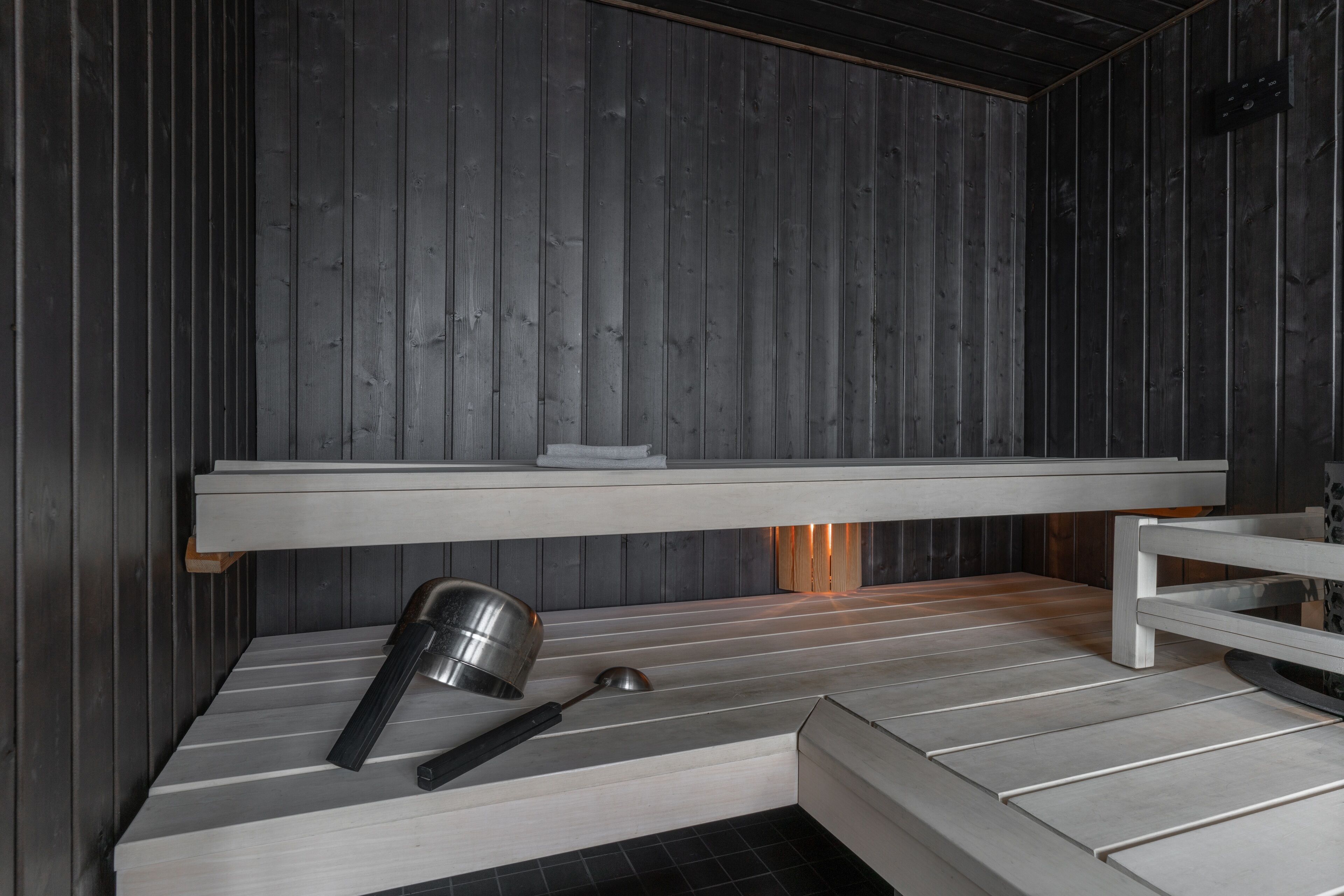 Uma sauna com interior em madeira, um banco e um balde de metal.