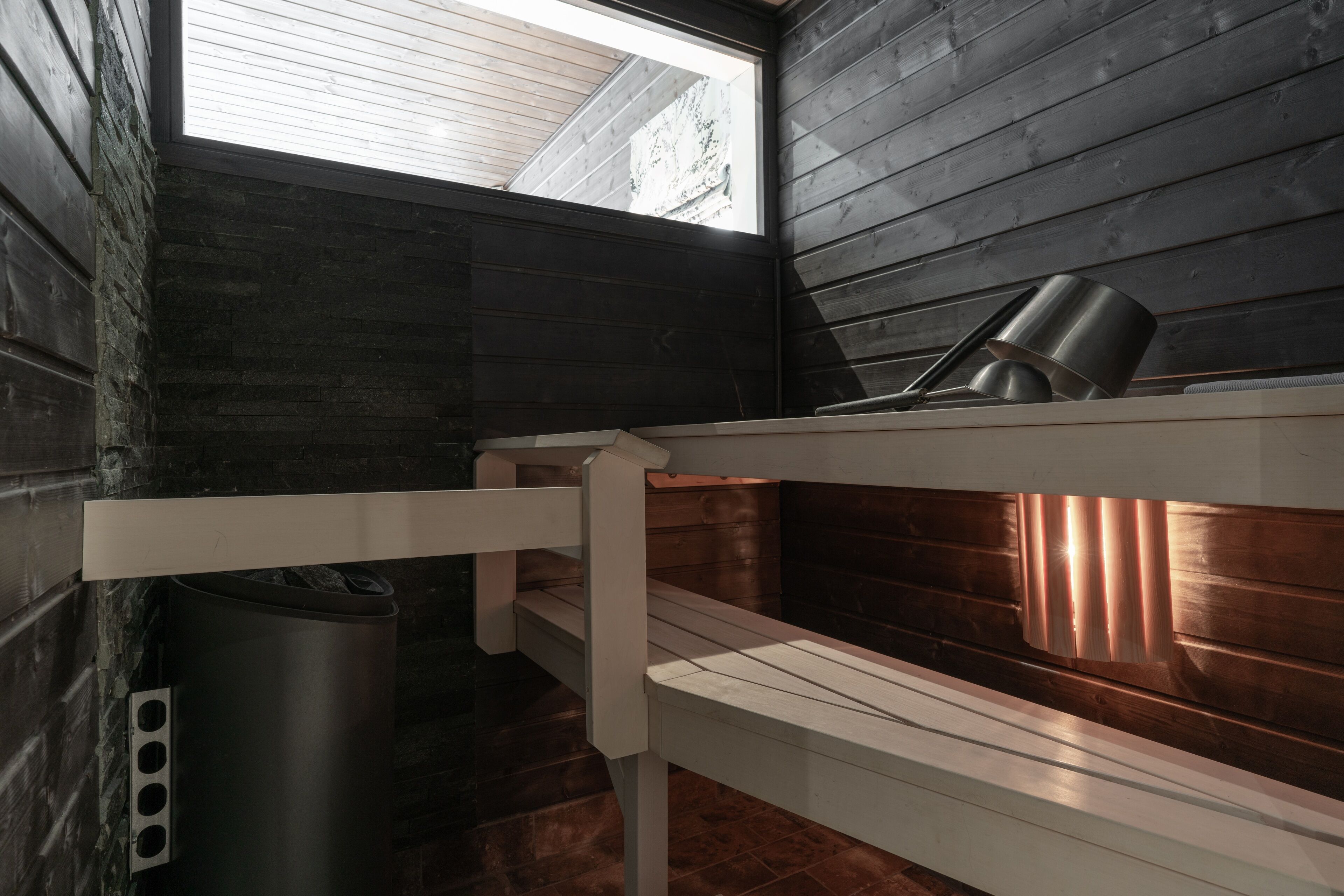 A bunk bed with a metal bucket and a trash can in a room with dark wooden walls and a skylight.