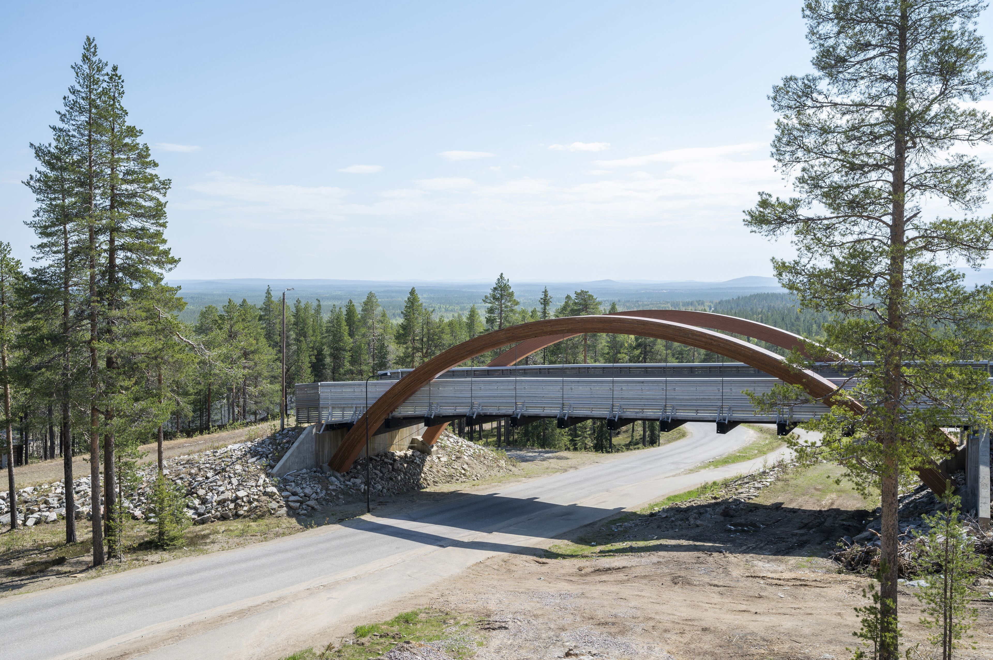 Un pont avec une arche incurvée enjambant une route, entouré d’arbres et sous un ciel dégagé.