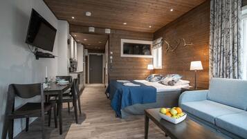 Quarto moderno com cama, sofá, mesa de jantar com cadeiras e TV fixada na parede.
