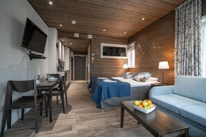 A modern room with a bed, a sofa, a dining table with chairs, and a TV mounted on the wall.