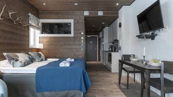 Ein modernes Hotelzimmer mit Holzboden, einem großen Bett mit blauer Bettwäsche, einem Schreibtisch mit Stuhl und einem an der Wand befestigten Fernseher.