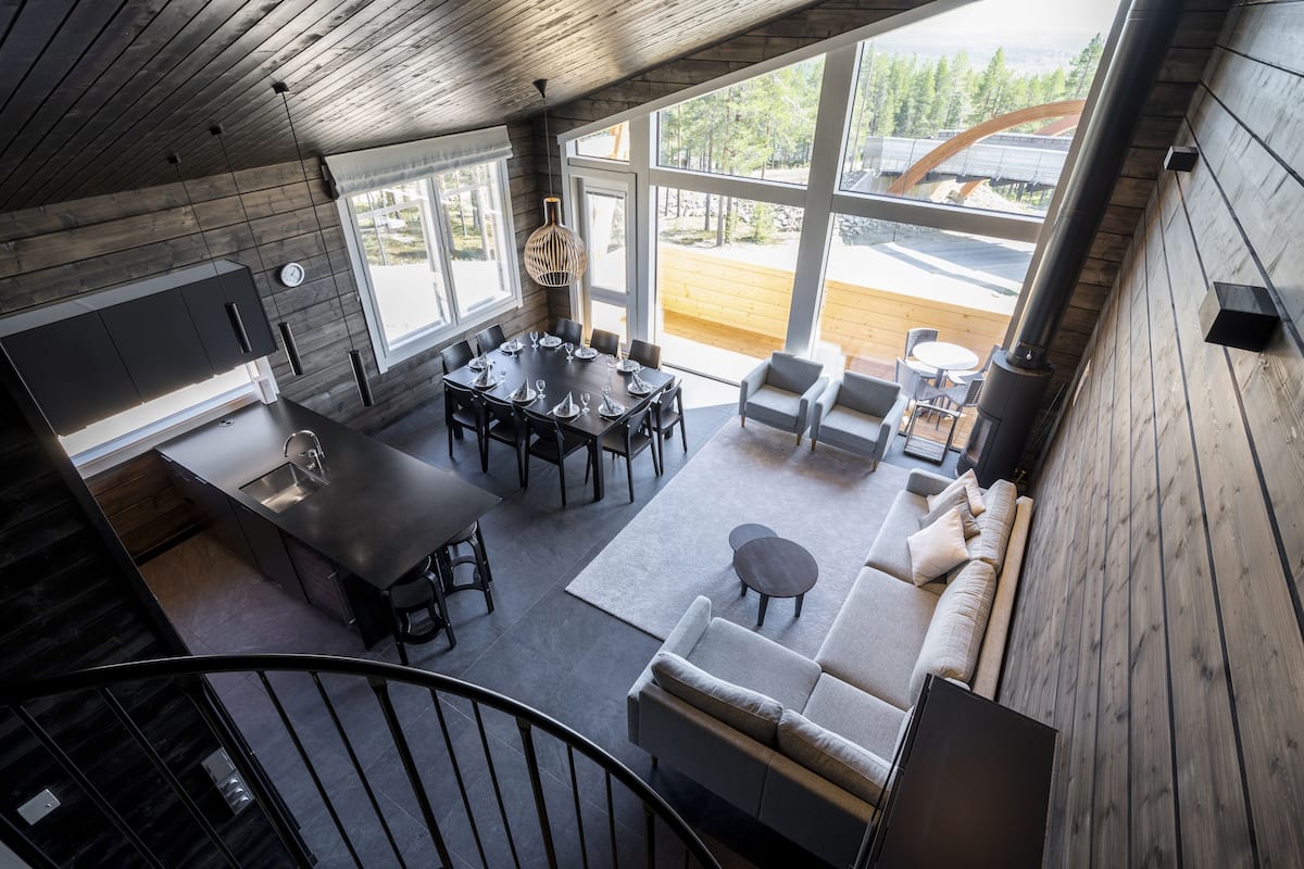 A modern interior with a dining area, sofa, and large windows offering a view of the outdoors.