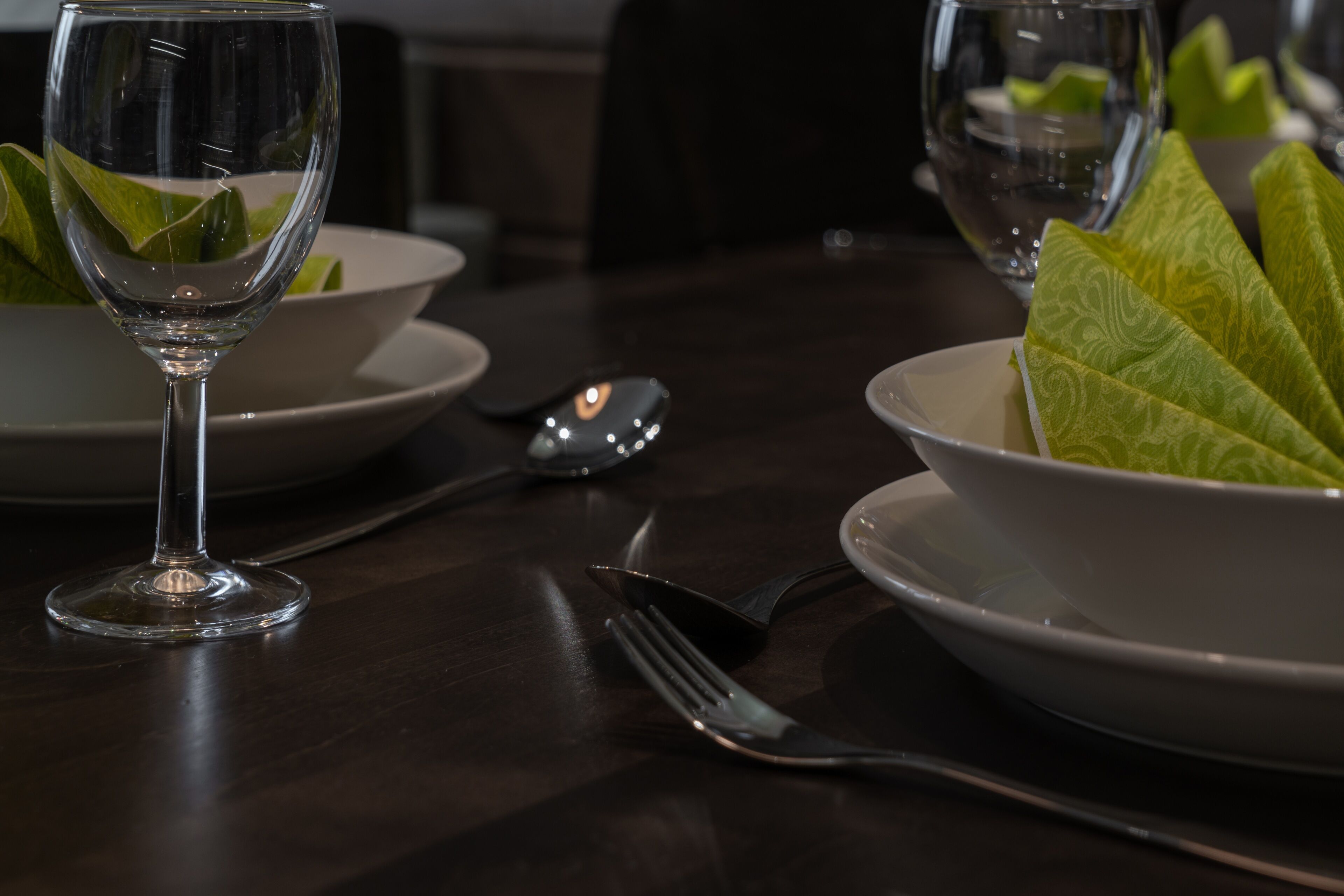 A dining table with a wine glass, a bowl of green leaves, and a fork and knife.
