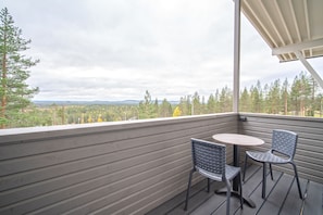 A balcony with a view of a forest and distant hills, featuring two chairs and a small round table.