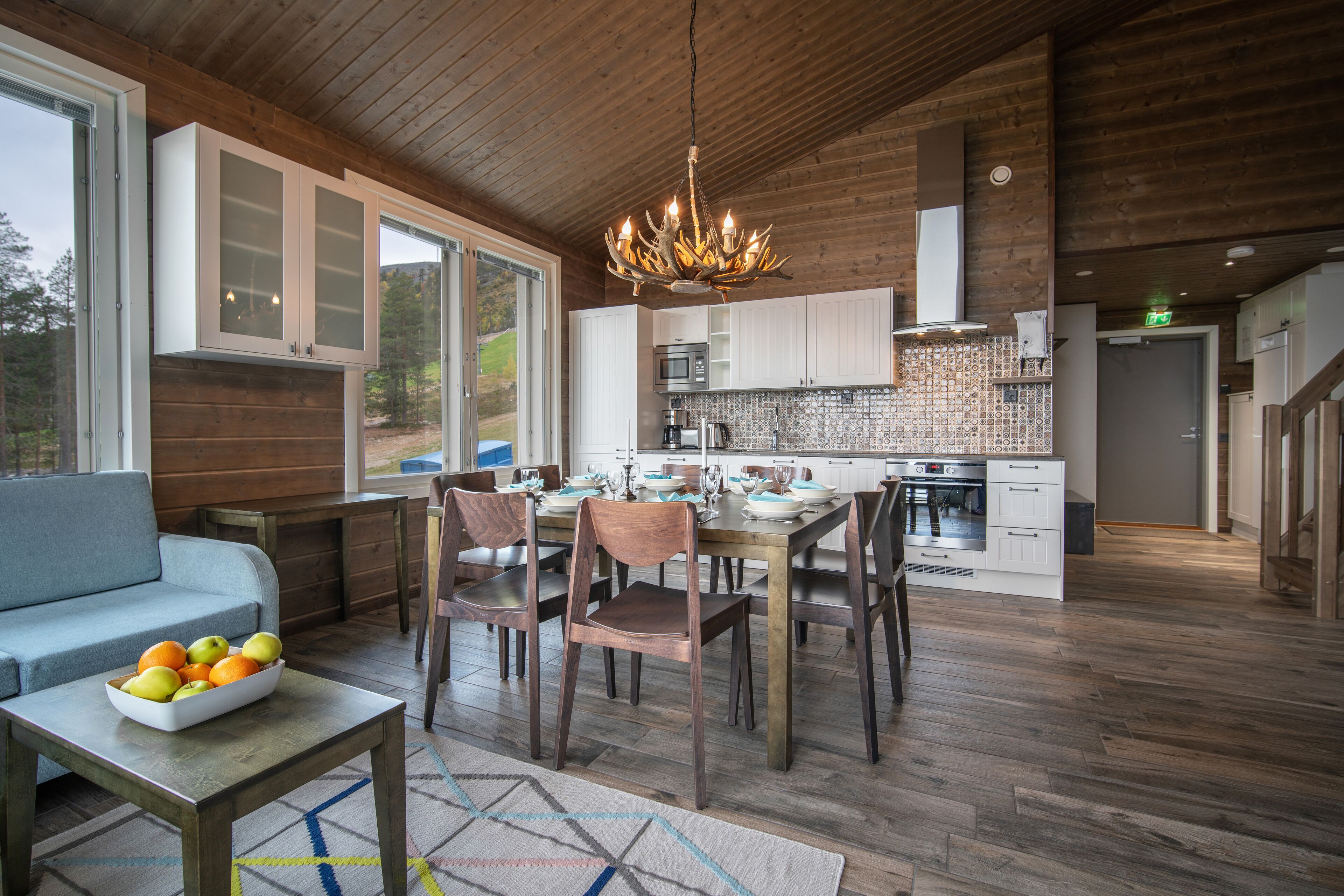A modern kitchen with wooden cabinets, a dining table with chairs, and a chandelier.