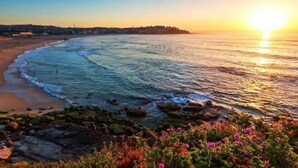 Vista de un atardecer costero con playa y primer plano rocoso.