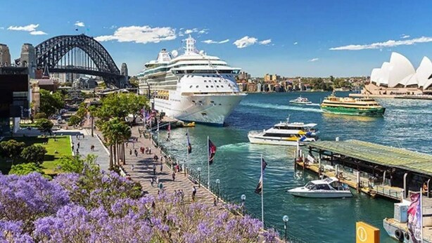 Un crucero amarrado en un puerto, con la Casa de la Ópera de Sídney y el Puente de Abordo al fondo.