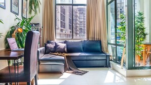 A modern living room with a sofa, a dining table, and a laptop. There are plants and curtains. - ★ Funky Surry Hills Warehouse by ★ Sydney Dreams ★ (Darlinghurst)