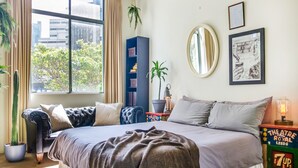 A bedroom with a large bed, a window with curtains, a bookshelf, a potted plant, and a lamp. - ★ Funky Surry Hills Warehouse by ★ Sydney Dreams ★ (Darlinghurst)