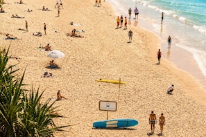 Ein Strand mit Personen, die sonnenbaden und schwimmen, einem Rettungsschwimmerstand und einem blauen Rettungsboot.