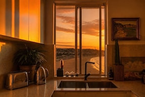 Una cocina con vista a un atardecer, un fregadero, un tostador, una cafetera y un cactus.