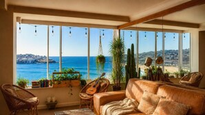 A cozy living room with a leather sofa, wicker chairs, a guitar, and a view of the sea.