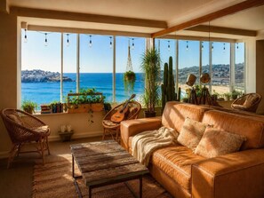 Ein gemütliches Wohnzimmer mit Ledersofa, Korbstühlen, einer Gitarre und Meerblick.