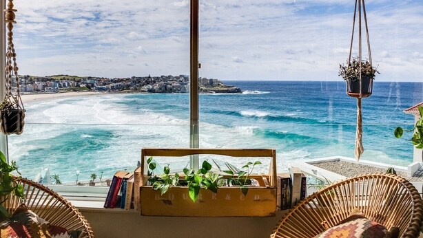 A coastal view with a bookshelf, hanging plants, and wicker furniture.