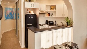 A compact kitchen with white cabinets, a black refrigerator, a stove, and a sink. There are potted plants and a world map on the wall. - ★ Sub-Penthouse Beach View ★ by Sydney Dreams ★ (Bondi Beach)