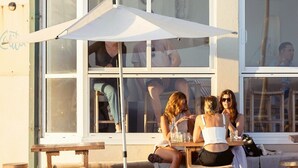 An outdoor seating area with tables and umbrellas, a building facade with windows, and a visible sign with the word 'Calito'. - ★ Sub-Penthouse Beach View ★ by Sydney Dreams ★ (Bondi Beach)
