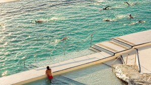 A swimming pool with clear water, a person in the water, and a lifeguard stand.
