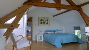 A bedroom with a sloped ceiling, a bed with blue bedding, a white chair, and a small bedside table.