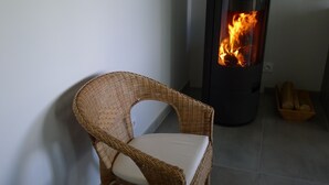 A wicker chair with a cushion in a room with a tiled floor and a wood-burning stove.