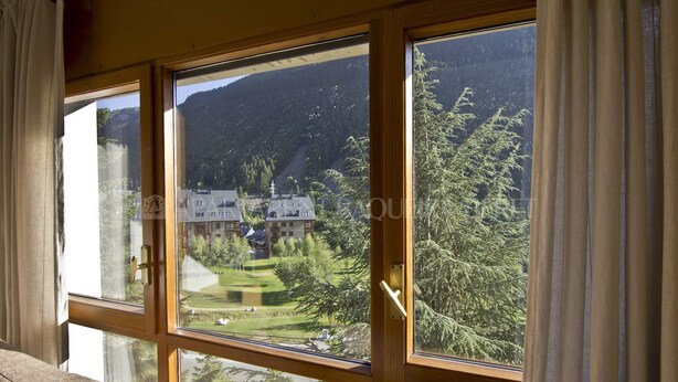 Una habitación con ventanas amplias que ofrecen vistas a un paisaje montañoso y un edificio de varios pisos.