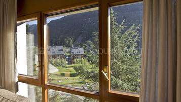 Una habitación con ventanas amplias que ofrecen vistas a un paisaje montañoso y un edificio de varios pisos.