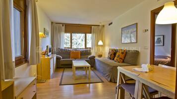 Una sala de estar acogedora con un sofá, una mesa de centro y una mesa de comedor. Hay una ventana con cortinas, una lámpara y un cuadro en la pared.