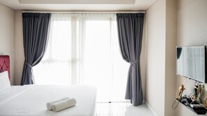 A hotel room with a bed, a TV, and curtains. - Cozy Minimalist Studio @ Casa de Parco Apartment (Pagedangan)
