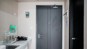 A modern bathroom with a dark door, a sink, and a dish rack. - Cozy Minimalist Studio @ Casa de Parco Apartment (Pagedangan)