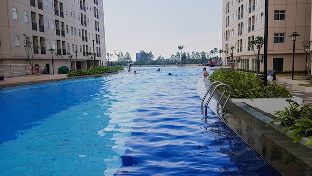 A swimming pool surrounded by apartment buildings, with people swimming and relaxing. - 2BR Apartment for 4 Pax at Ayodhya Residences (Tangerang)
