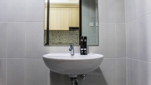 Een badkamer met een witte wastafel, een spiegel en twee zwarte flessen op de wastafel.