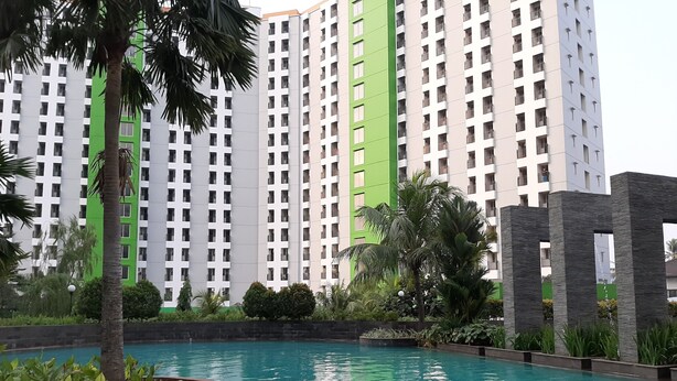 A swimming pool with a clear blue water surface, surrounded by a landscaped area with palm trees and shrubs. In the background, there are high-rise residential buildings with balconies.
