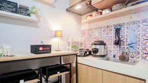 A compact kitchen with a coffee machine, kettle, and a hanging pot rack.